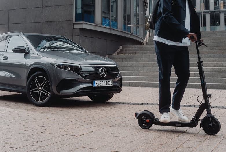Czarna hulajnoga elektryczna Mercedes-AMG obok samochodu Mercedes-Benz na miejskim placu.