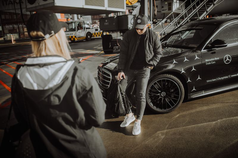 Mężczyzna w kurtce Mercedes-Benz przy sportowym samochodzie.